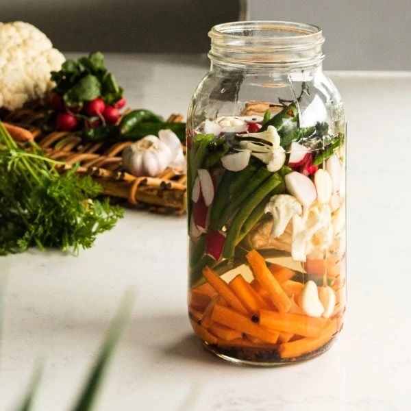 Glasburk med skivade grönsaker och rotfrukter för fermentering