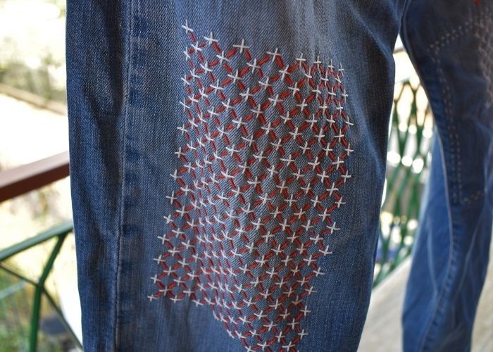 Närbild av jeans med dekorativa sashikostygn i rött och vitt