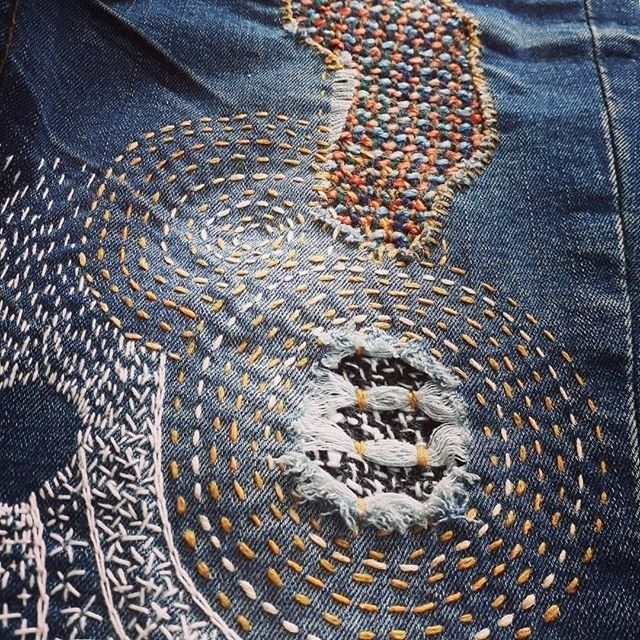 Närbild av slitna jeans lagade med färgstarka sashikostygn